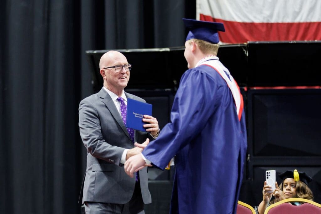 Greg West presenting a diploma to a graduate.